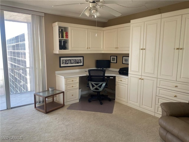 carpeted office space featuring built in desk and ceiling fan