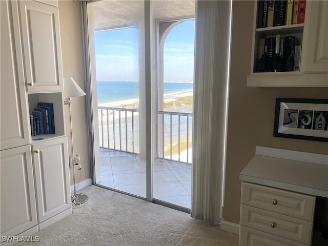 doorway to outside with a water view, light colored carpet, and a view of the beach