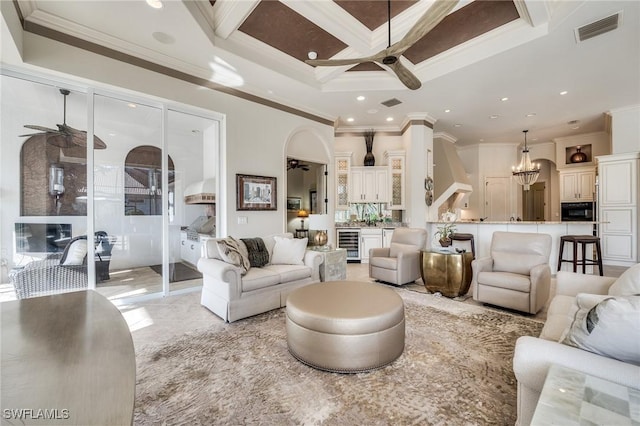 living room with ornamental molding, coffered ceiling, ceiling fan with notable chandelier, and wine cooler