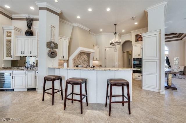 kitchen featuring white cabinetry, a breakfast bar area, beverage cooler, hanging light fixtures, and light stone countertops