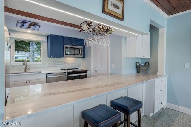 kitchen featuring sink, blue cabinetry, backsplash, stainless steel appliances, and a kitchen breakfast bar