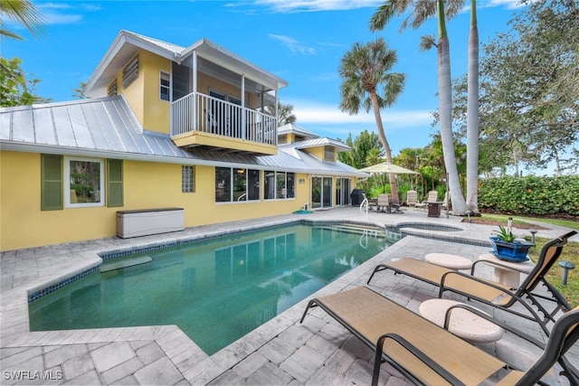 rear view of house with a balcony, a patio area, and a pool with hot tub