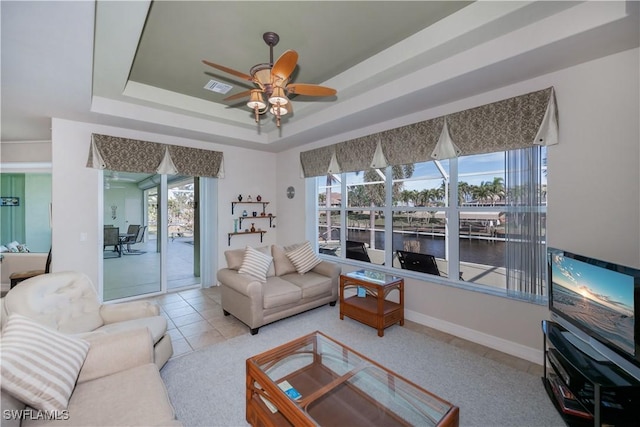 tiled living room with ceiling fan and a tray ceiling