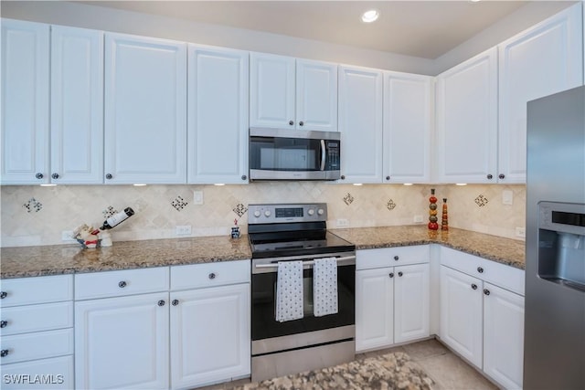 kitchen featuring appliances with stainless steel finishes, white cabinetry, backsplash, light tile patterned flooring, and dark stone counters