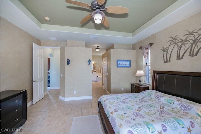 tiled bedroom featuring ceiling fan, a raised ceiling, and ensuite bath