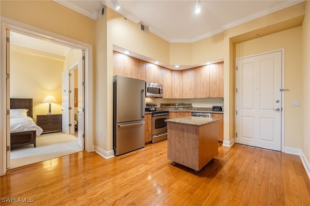 kitchen featuring a high ceiling, appliances with stainless steel finishes, a center island, ornamental molding, and light hardwood / wood-style flooring