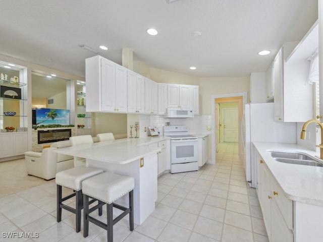 kitchen featuring white appliances, white cabinetry, sink, kitchen peninsula, and a breakfast bar area