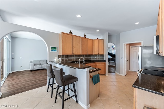 kitchen with light tile patterned flooring, stainless steel refrigerator, kitchen peninsula, dark stone counters, and backsplash