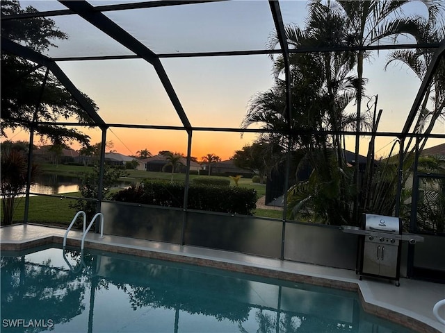 pool at dusk with grilling area, a water view, and glass enclosure