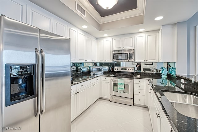 kitchen with sink, a tray ceiling, white cabinetry, appliances with stainless steel finishes, and dark stone counters