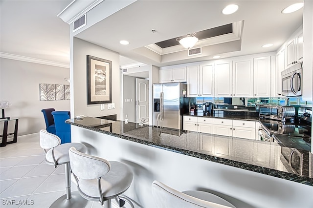 kitchen with a kitchen bar, kitchen peninsula, stainless steel appliances, a tray ceiling, and white cabinets