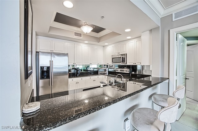 kitchen with white cabinets, kitchen peninsula, a tray ceiling, and stainless steel appliances