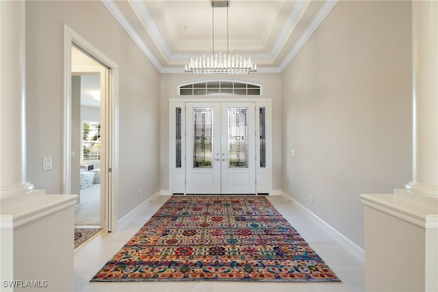 foyer with crown molding, a tray ceiling, a chandelier, and decorative columns