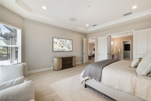 bedroom with a spacious closet, a tray ceiling, ensuite bathroom, and light wood-type flooring