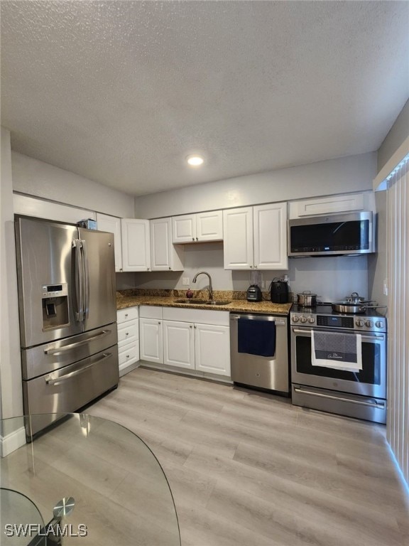 kitchen with a textured ceiling, white cabinets, appliances with stainless steel finishes, light hardwood / wood-style floors, and sink