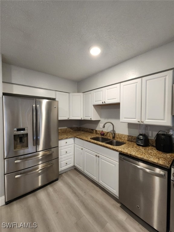 kitchen with white cabinetry, stainless steel appliances, dark stone countertops, a textured ceiling, and sink