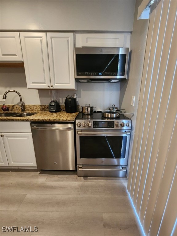 kitchen with dark stone counters, sink, stainless steel appliances, and white cabinetry