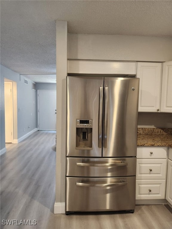 kitchen featuring light hardwood / wood-style floors, dark stone counters, a textured ceiling, white cabinets, and stainless steel fridge