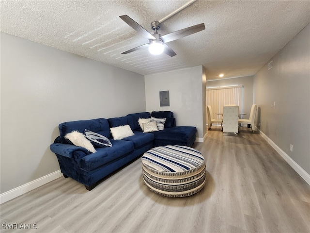 living room featuring a textured ceiling, ceiling fan, electric panel, and light hardwood / wood-style flooring