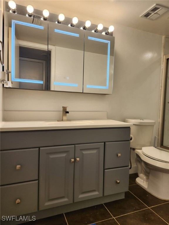 bathroom with toilet, tile patterned floors, vanity, and a shower with shower door