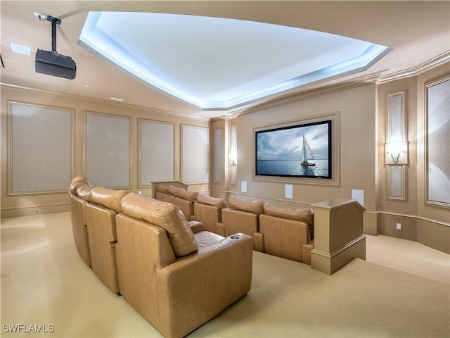 carpeted home theater room with ornamental molding and a tray ceiling