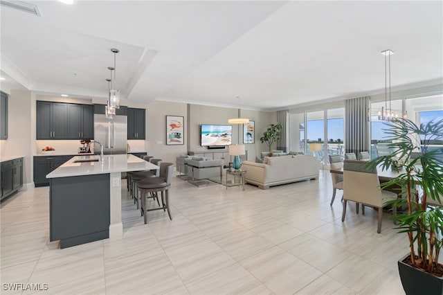 kitchen featuring sink, a breakfast bar area, built in refrigerator, hanging light fixtures, and a center island with sink