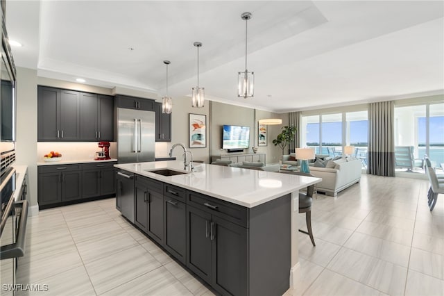 kitchen with sink, an island with sink, a kitchen bar, decorative light fixtures, and a raised ceiling