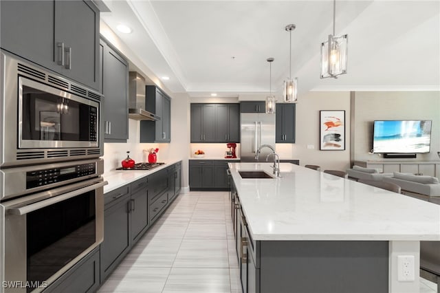 kitchen with an island with sink, wall chimney exhaust hood, built in appliances, and sink