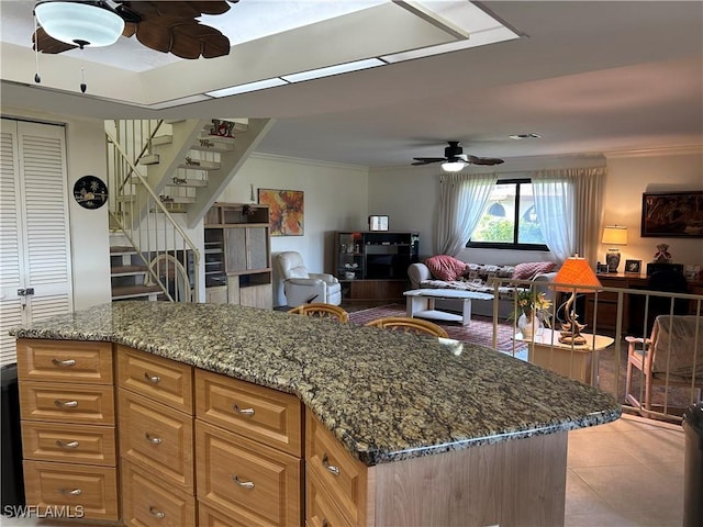 kitchen featuring light tile patterned flooring, a kitchen island, stone countertops, ceiling fan, and crown molding