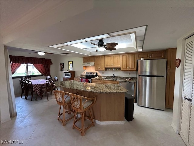 kitchen featuring a kitchen bar, a center island, appliances with stainless steel finishes, a tray ceiling, and ceiling fan