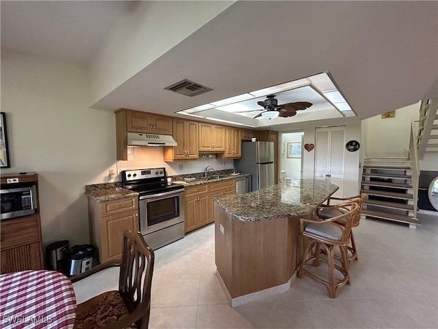 kitchen featuring ceiling fan, stainless steel appliances, a center island, and dark stone counters