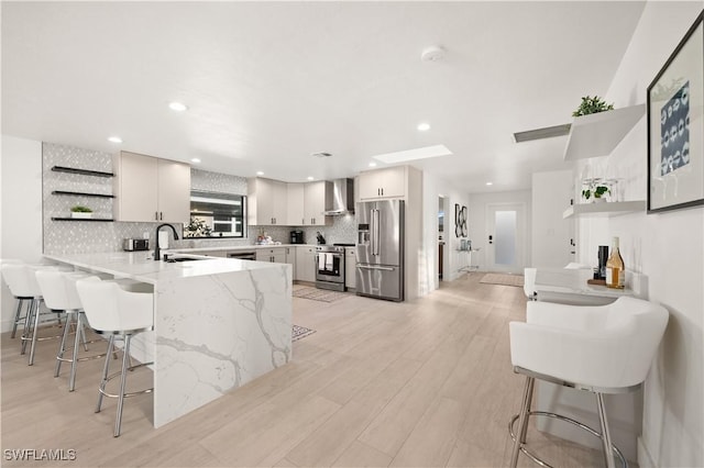 kitchen featuring wall chimney exhaust hood, a breakfast bar, kitchen peninsula, and appliances with stainless steel finishes