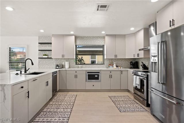 kitchen featuring appliances with stainless steel finishes, wall chimney range hood, light hardwood / wood-style floors, sink, and backsplash