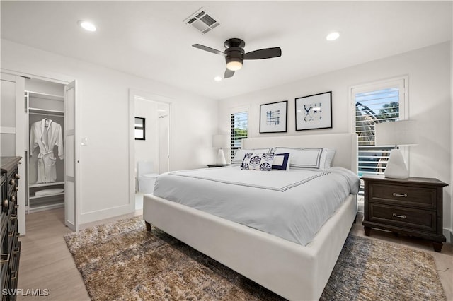 bedroom featuring ensuite bath, multiple windows, a closet, light wood-type flooring, and ceiling fan