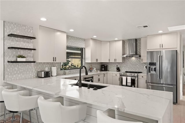 kitchen with a kitchen breakfast bar, kitchen peninsula, premium appliances, light stone counters, and wall chimney range hood