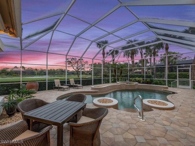 pool at dusk featuring an outdoor fire pit, a patio area, an in ground hot tub, and glass enclosure
