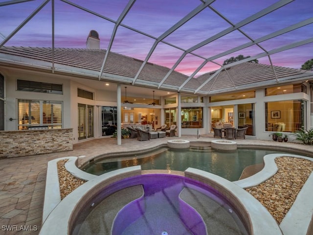 pool at dusk featuring a lanai, an in ground hot tub, ceiling fan, an outdoor hangout area, and a patio