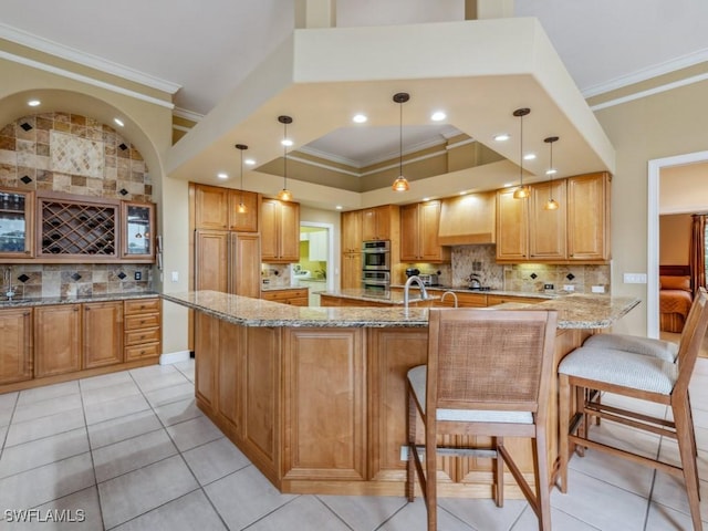 kitchen featuring decorative light fixtures, a kitchen breakfast bar, light stone counters, crown molding, and wall chimney range hood