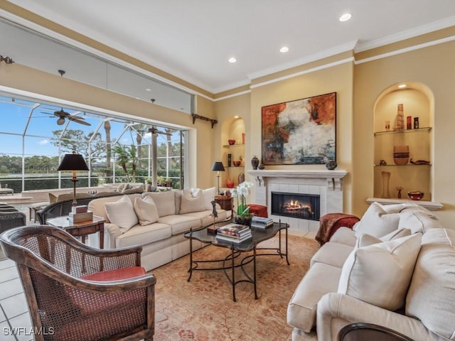 living room featuring a tile fireplace, ornamental molding, built in features, and ceiling fan