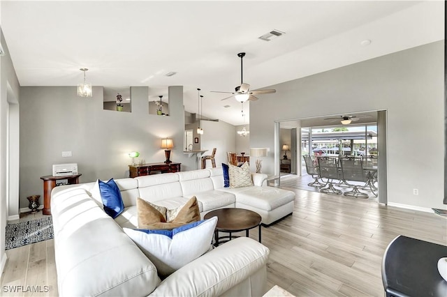 living room with ceiling fan with notable chandelier, light hardwood / wood-style flooring, and lofted ceiling