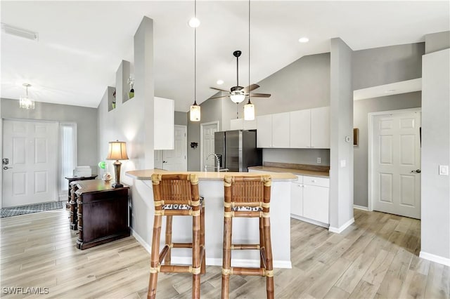 kitchen with kitchen peninsula, stainless steel fridge, white cabinets, high vaulted ceiling, and a breakfast bar area