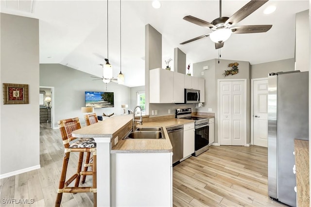 kitchen with kitchen peninsula, appliances with stainless steel finishes, sink, white cabinets, and a kitchen bar