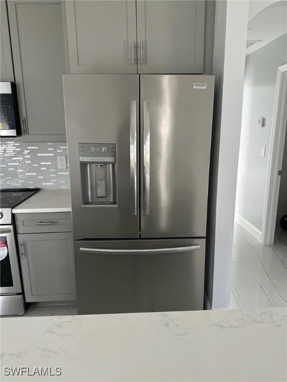 kitchen with light stone counters, backsplash, gray cabinets, and stainless steel appliances