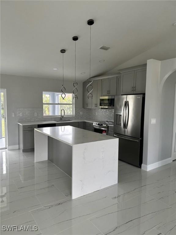 kitchen with lofted ceiling, a kitchen island, sink, gray cabinetry, and stainless steel appliances