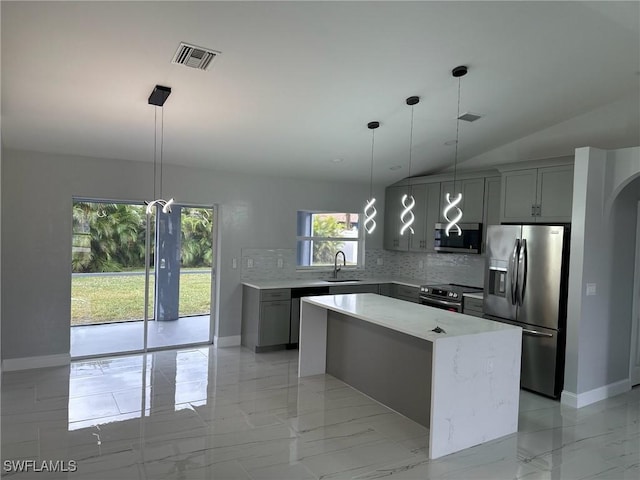 kitchen featuring decorative backsplash, gray cabinetry, stainless steel appliances, and a center island