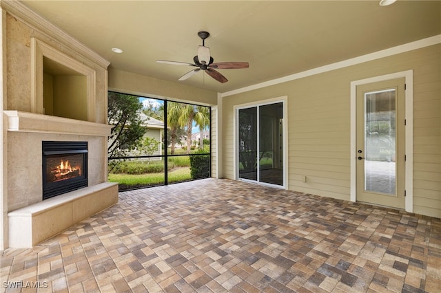 unfurnished sunroom with ceiling fan and an outdoor fireplace