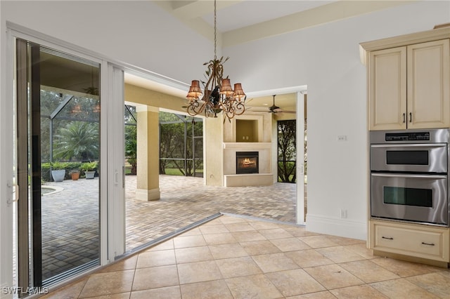 kitchen featuring light tile patterned floors, cream cabinetry, decorative light fixtures, double oven, and ceiling fan with notable chandelier