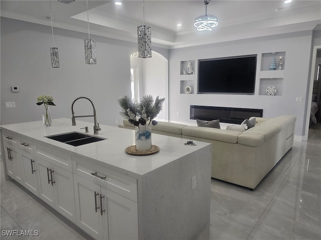 kitchen featuring pendant lighting, sink, a tray ceiling, an island with sink, and white cabinets