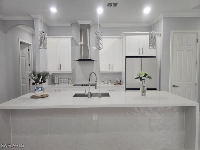 kitchen with white cabinetry, wall chimney range hood, white fridge, and an island with sink