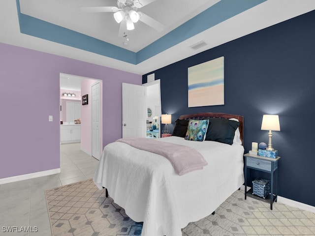 bedroom featuring ceiling fan, a raised ceiling, ensuite bath, and light tile patterned floors